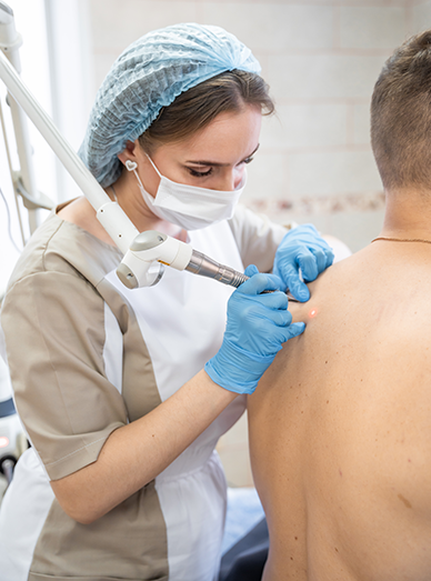 Clinician examining a patient’s back with a dermatology device at Mambourin Doctors.